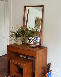 a wooden desk with a mirror on top of it next to a chair and potted plant