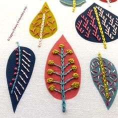 four different types of embroidered leaves on a white cloth with red, blue and yellow thread