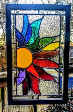 a colorful stained glass sunflower sitting on top of a wooden bench in front of trees