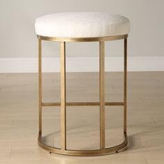 a round stool with a gold frame and white upholstered cushion on the top