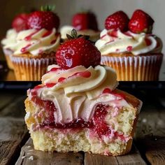 two cupcakes with white frosting and strawberries on top are sitting on a wooden table