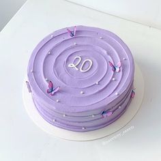 a purple cake with butterflies on it sitting on top of a white table next to a cupcake