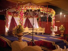 a decorated stage set up for a wedding ceremony with flowers on the ceiling and drapes