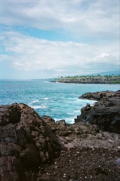 an ocean view with rocks and blue sky in the foreground, and houses on the other side