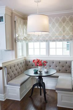 a corner table with two chairs and a bench in front of the window, next to a white couch