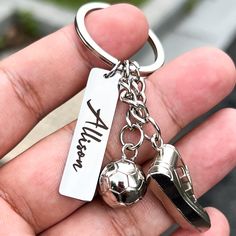 a hand holding a silver key chain with two shoes and a ball on it that says william