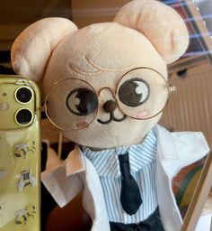 a teddy bear wearing glasses and a tie next to a cell phone with an eye patch on it