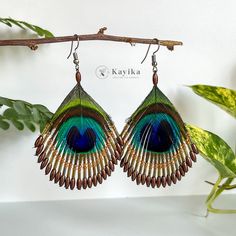 a pair of peacock feather earrings hanging from a branch