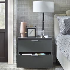 a nightstand with a clock and lamp on it next to a bed