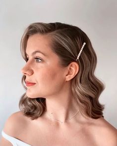 a woman wearing a white dress with a pearl hair clip on her head, looking off to the side