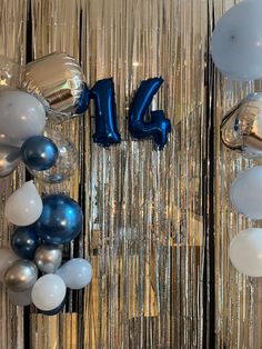 balloons and streamers in the shape of numbers are hanging on a wall that is decorated with metallic foil