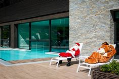 two people dressed as santa claus sitting in lawn chairs next to a swimming pool,