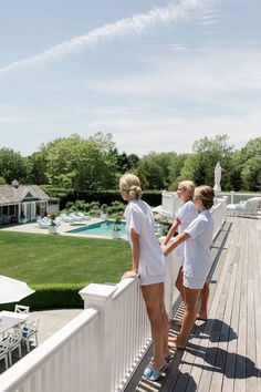 three women standing on a deck looking at the pool and surrounding area that is fenced in