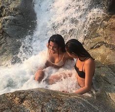 two women are sitting in the water near a waterfall