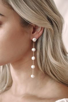 a woman with blonde hair wearing white pearls on her ear and earrings, looking at the camera