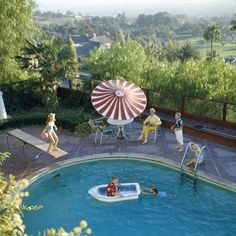 an outdoor swimming pool with people playing in the water and on lounge chairs around it