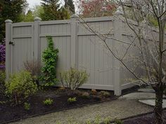 a fence that is next to a tree and bushes in the yard with flowers growing on it