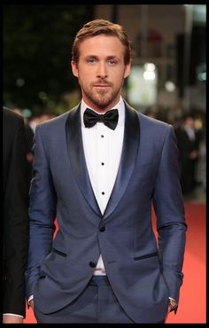 a man in a tuxedo and bow tie standing next to another man on a red carpet