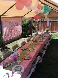 a table set up for a baby shower with pink and green plates, napkins and balloons