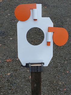 an orange and white object sitting on top of a wooden post in the middle of gravel