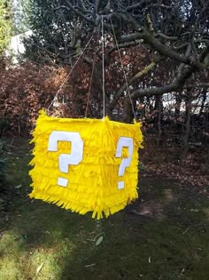 a yellow object with white letters hanging from it's sides in the grass next to a tree