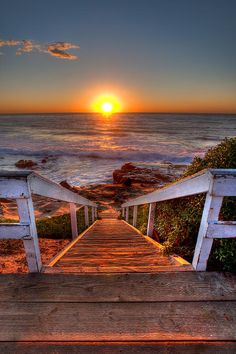 the sun is setting over the ocean with steps leading to it and an orange sky in the background