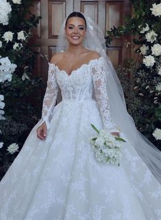 a woman in a wedding dress standing next to a flower covered wall with white flowers