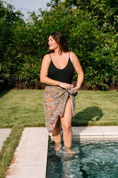 a woman in a black tank top and floral skirt standing by the edge of a pool