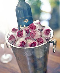 a metal bucket filled with ice and roses next to a bottle of wine on top of a wooden table