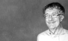 black and white photo of an older man with glasses smiling at the camera, in front of a gray background