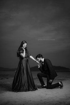 a man kneeling down next to a woman on top of a sandy beach under a cloudy sky