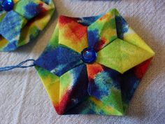 two colorful origami pieces are sitting on a table with blue beads and thread