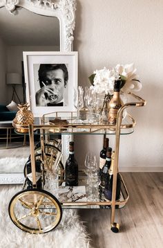 a gold bar cart with wine glasses and bottles on it in front of a mirror