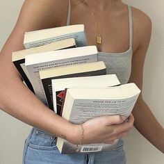 a woman holding a stack of books in her hands while wearing a tank top and jeans