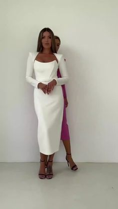 a woman standing in front of a white wall wearing a long sleeved dress and heels