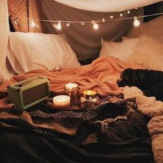 a dog laying on top of a bed covered in blankets next to candles and lights