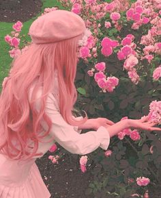 a woman with long pink hair is standing in front of flowers and holding out her hand