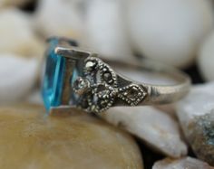 This is the perfect option for those who like cool, unique jewelry and the luxury, shine of silver,light blue. This ring is well made, cute and/or elegant in design, and very desirable. The ring is decorated with clear light blue stone in the sterling bezels. The ring is decorated with cz on the sides, but almost all cz are lost. ♥ There is a hallmark: 925. ♥The ring is in very good condition. ♥The size of the ring is 5 1/4. ♥The band of ring is curved. This item is pre-owned vintage and may sho Blue Rectangular Topaz Jewelry, Silver Ring With Rectangular Blue Topaz, Silver Rings With Rectangular Blue Topaz, Silver Topaz Ring With Rectangular Blue Stone, Silver Blue Topaz Ring With Rectangular Stone, Silver Rectangular Topaz Ring, Rectangular Silver Blue Topaz Ring, Rectangular Silver Topaz Ring, Blue Rectangular Topaz Ring With Accent Stones