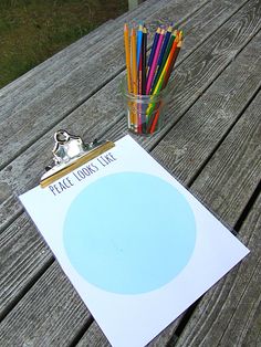 there is a glass with colored pencils next to a piece of paper on the table