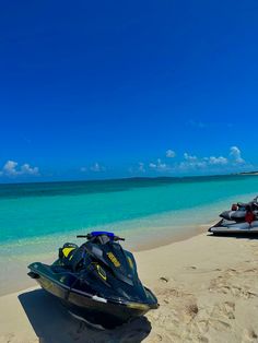 two jet skis are parked on the beach next to the blue water and white sand