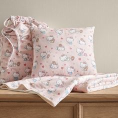 two hello kitty pillow cases sitting on top of a wooden dresser next to a drawstring bag