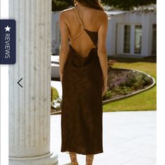 a woman in a brown dress standing next to a pillar and looking at the ground