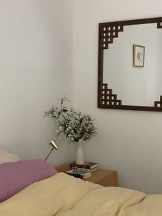 a bed sitting under a mirror next to a table with a vase on top of it