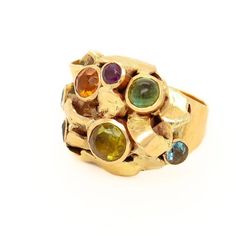 A fine Modernist ring.  By the New York City Modernist female goldsmith Resia Schor.   In 14k gold with multi-gemstones.  Comprising a Brutalist head with varied gold elements and bezel-set gemstones. Set with an oval emerald cabochon, a green tourmaline, aquamarines, citrines, and amethysts on a hand-built tapered shank.  Designed with stylistic elements of the work of Resia's husband, Ilya Schor, Cubism, and Brutalism. Incorporating these elements in addition to a strong nod to the design of a Modern Gold Multi-stone Gemstones, Gold Multi-stone Gemstones, Unique Multi-stone Gold Gemstones, Modern Multicolored Multi-stone Gemstones, Modernist Multi-stone Ring, Emerald Cabochon, Modernist Ring, Aqua Marine, Brutalism