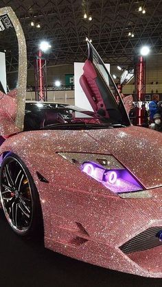 a pink car covered in lots of sparkles at an auto show with its doors open