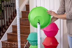 a woman is holding three large plastic bowls in front of stairs and railings, while another person stands next to the staircase