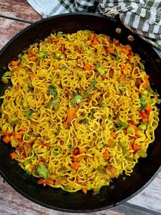 a pan filled with noodles and vegetables on top of a wooden table