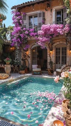 an outdoor swimming pool surrounded by flowers and potted plants in front of a house