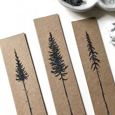 three pieces of paper with trees drawn on them next to some paintbrushes and other items