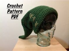 a crocheted green hat on top of a glass head mannequin's head